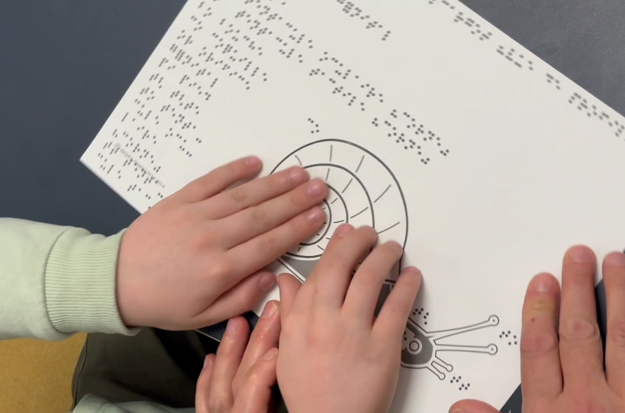 Des mains d'enfants explorent l'image tactile d'un escargot 