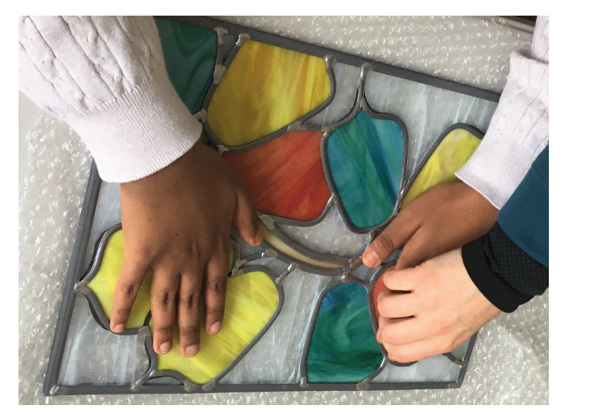 Mains touchant un vitrail.