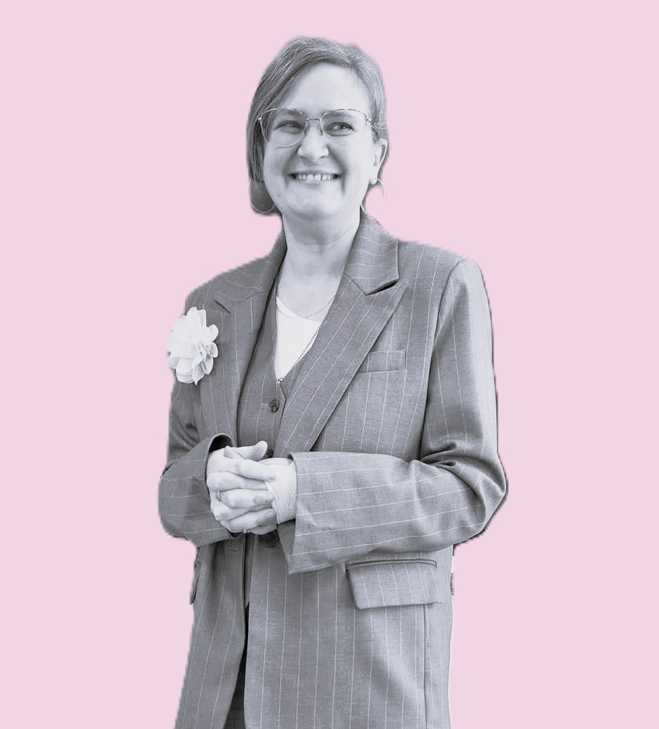 Photo de Marie-Pierre Toubhans en noir et blanc sur fond rose pâle. En tailleur, elle porte une fleur blanche sur le revers de veste